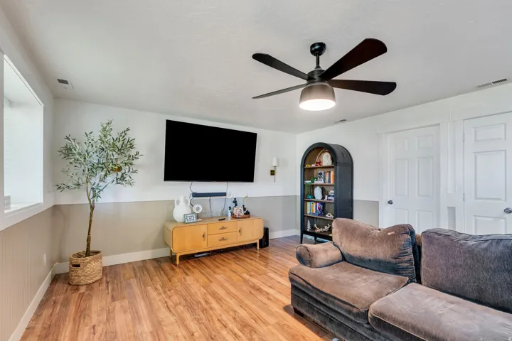 Spacious room with wood-finish flooring, a contemporary ceiling fan with integrated lighting, and two-tone wall paneling