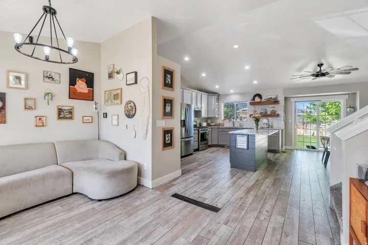 Open-concept living area featuring wood-finish flooring, a modern kitchen island with seating, stainless steel appliances, and a sliding glass door