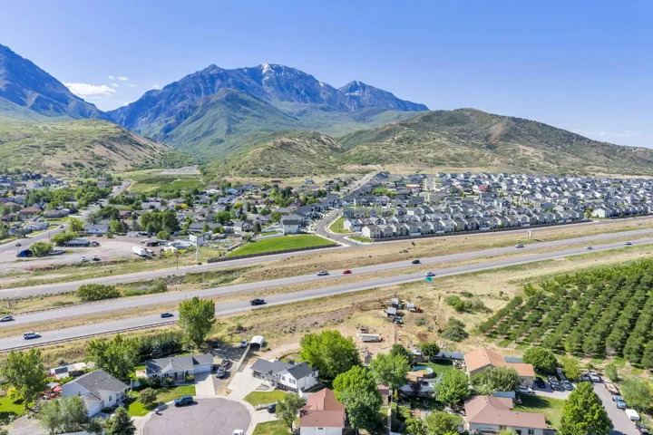 Expansive aerial perspective showcasing a mountainous backdrop, a multi-lane highway, and surrounding residential communities