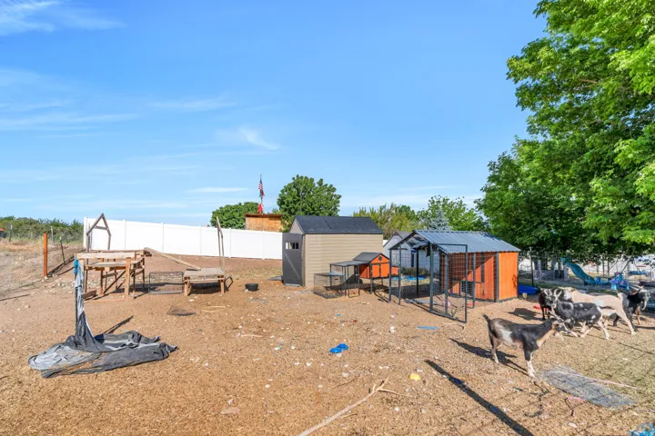 Expansive outdoor space featuring a white privacy fence, two utility sheds, and multiple animal enclosures