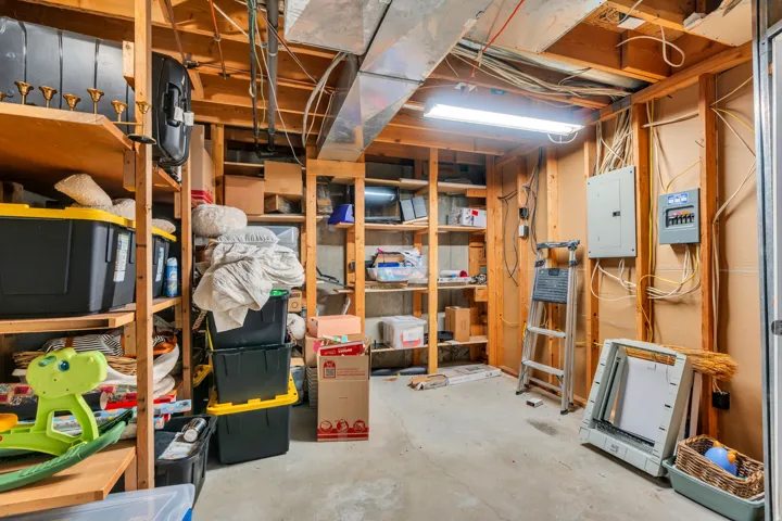 Unfinished basement space featuring exposed wood framing, concrete flooring, fluorescent lighting, built-in shelving, and exposed utility infrastructure