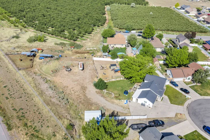 Aerial perspective showcasing a residential property with a dark shingle roof and light-colored siding, featuring a paved driveway and mature trees