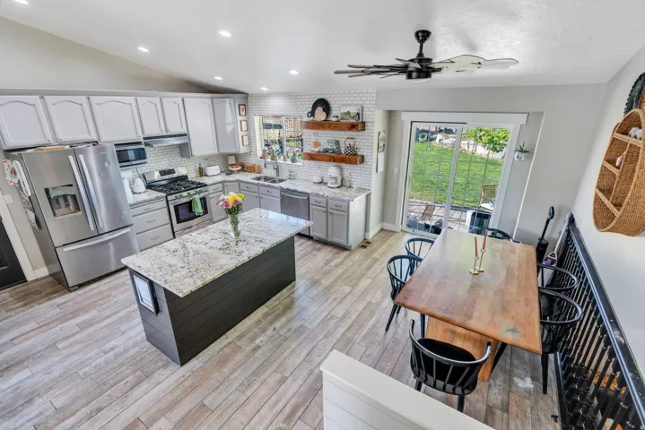 Open-concept kitchen and dining area featuring light wood-finish flooring, a kitchen island with a stone countertop, grey shaker-style cabinetry, and stainless steel appliances