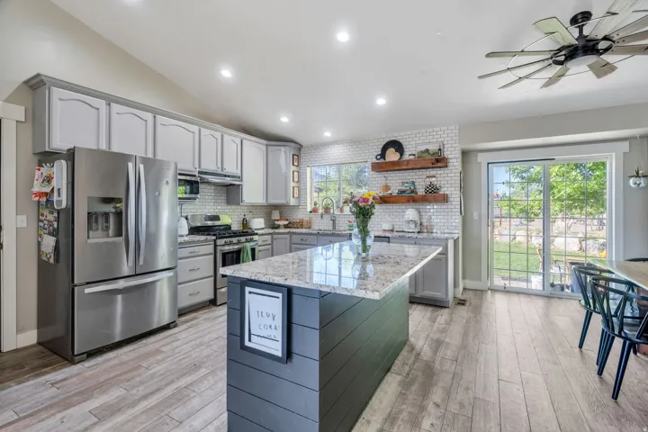 Spacious kitchen featuring an expansive center island with a granite countertop, wood-finish flooring, white subway tile backsplash, and stainless steel appliances