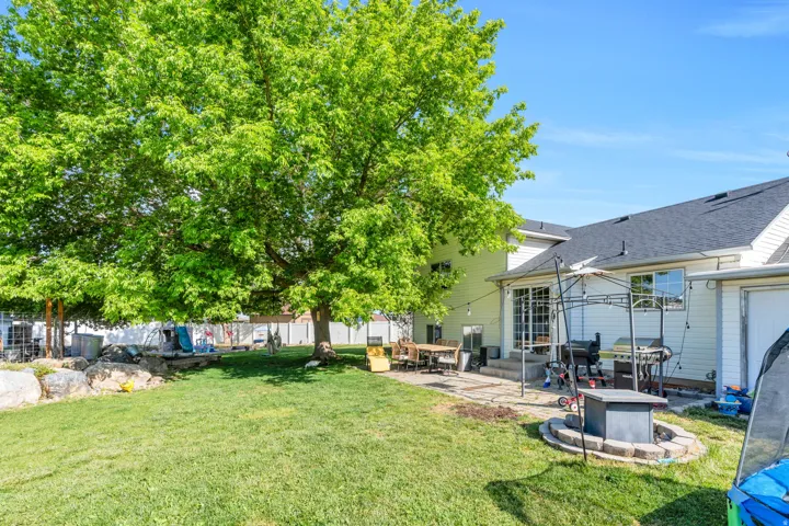 Expansive backyard featuring a large tree, a stone retaining wall, and a multi-level paver patio