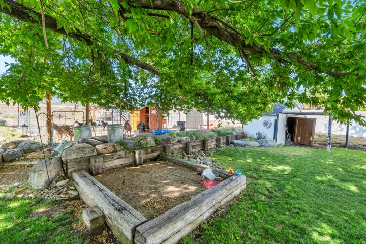 Expansive outdoor area featuring a mature tree canopy, green lawn, and a sand pit framed by railroad ties