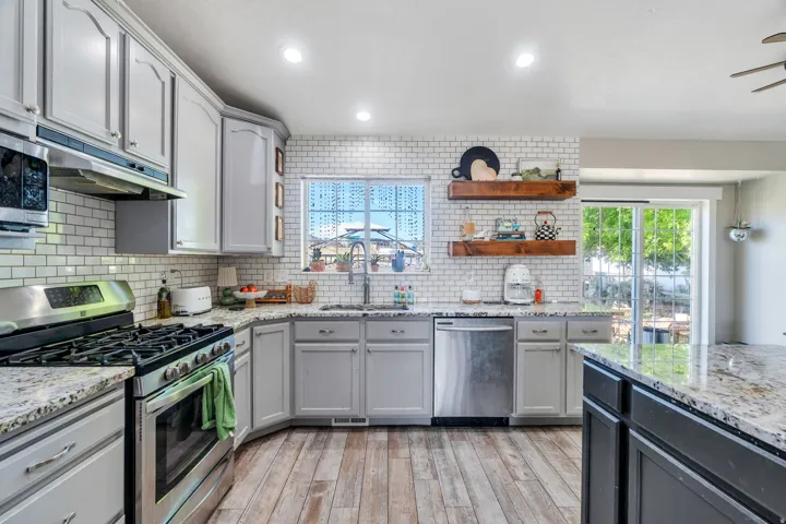 Kitchen featuring light gray cabinetry, stainless steel appliances, a subway tile backsplash, granite countertops, and wood-finish flooring