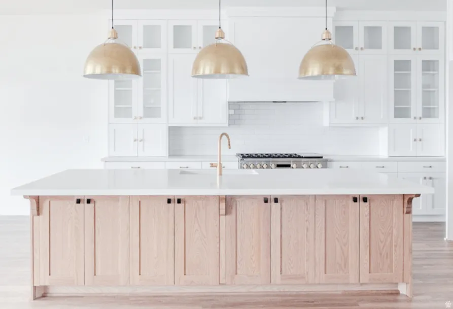 Kitchen island with light wood-finish cabinetry, white countertop, and three brass dome pendant lights