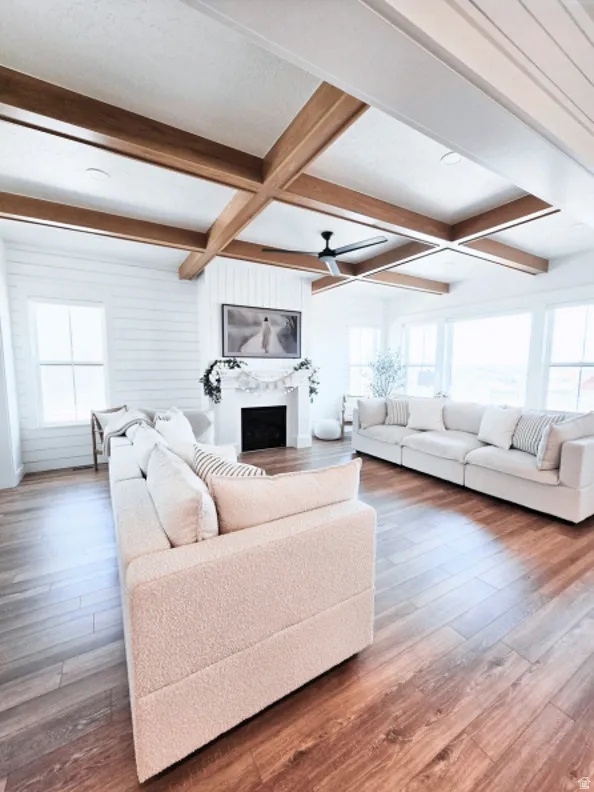 Spacious living area featuring coffered ceilings with exposed wood beams, wood-finish flooring, and a fireplace with a white mantel