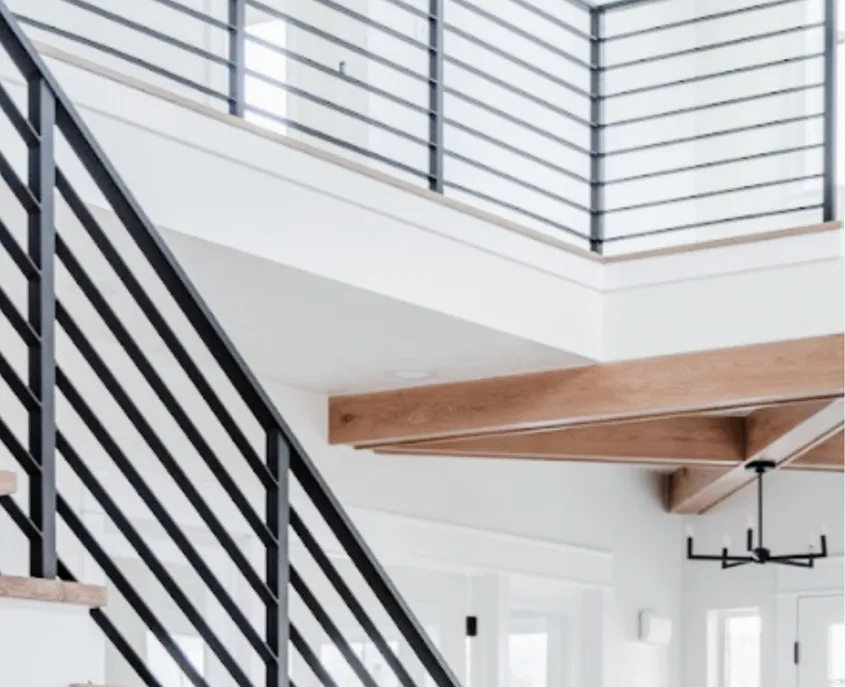 Open-concept interior featuring a wrought iron and wood-finish staircase, matching upper-level railing, exposed wood beams, and a black linear chandelier