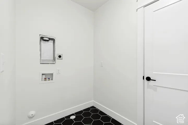 Laundry area featuring black hexagonal floor tiles, white baseboards, and a white flat-panel door with matte black hardware