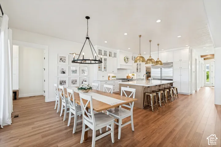 Open-concept kitchen and dining area featuring wood-finish flooring, white cabinetry, a large central island with seating, stainless steel appliances, and recessed lighting
