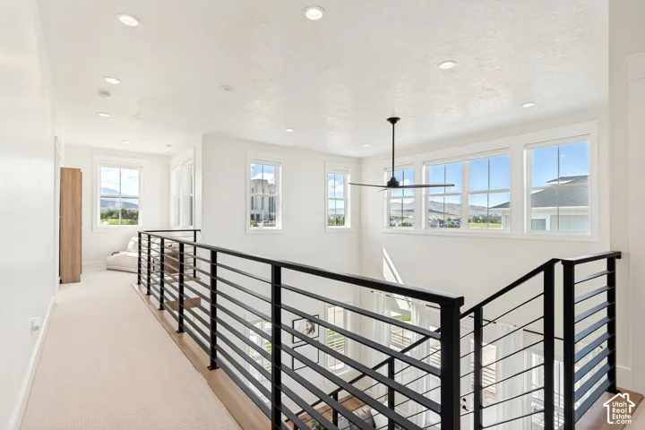 Upper-level hallway with modern black horizontal bar railing, recessed lighting, and a ceiling fan