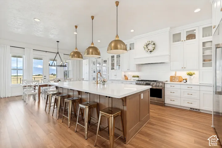 Gourmet kitchen featuring a large central island with seating, white shaker cabinetry, stainless steel appliances, and wood-finish flooring