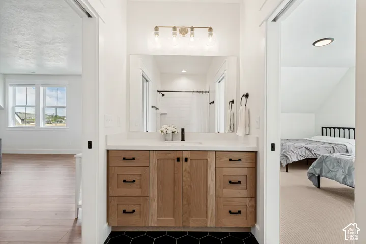 Guest loft bathroom vanity featuring a wood-finish cabinet with black hardware, white countertop, and black hexagonal floor tiles