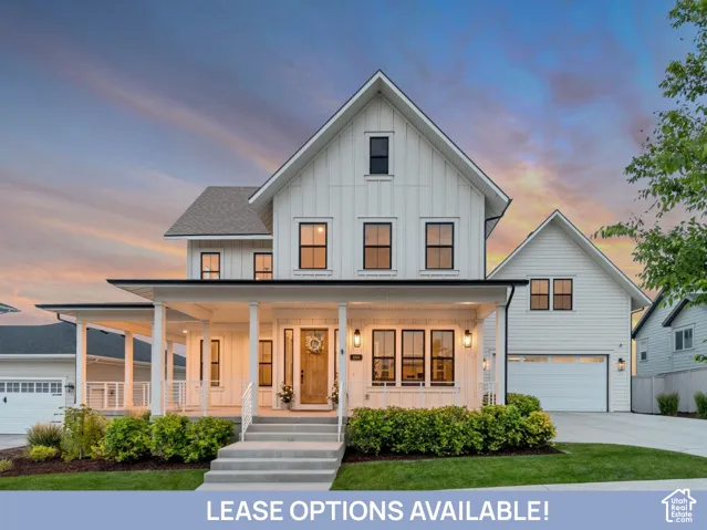 Two-story exterior featuring white vertical siding, a covered front porch with white railing, a wood-finish front door, and a multi-car garage