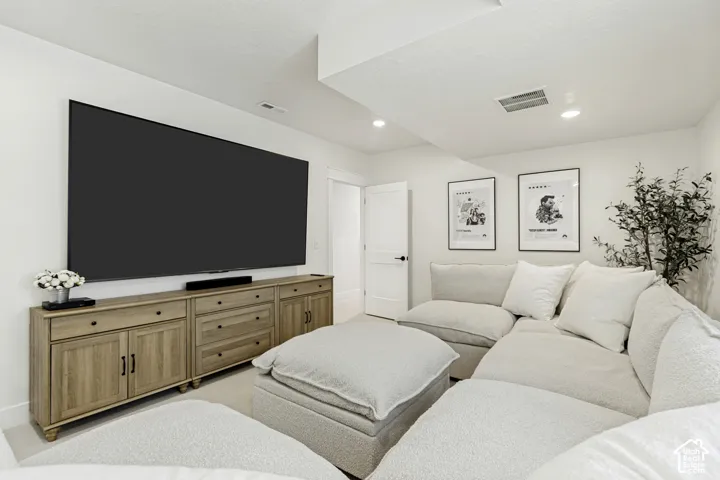 Entertainment area featuring a large wall-mounted screen, recessed ceiling lighting, a wood-finish media console with cabinet storage and drawers, and a white interior door with dark hardware