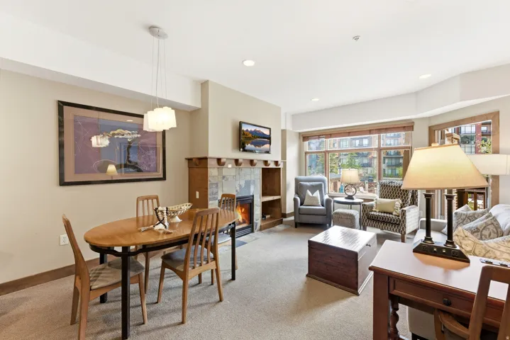 Open-concept living area featuring a stone-faced fireplace with wood mantel, large window array, recessed lighting, and a modern dining pendant light fixture