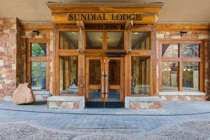 Stone facade with prominent wood beam accents and a central glass entry system