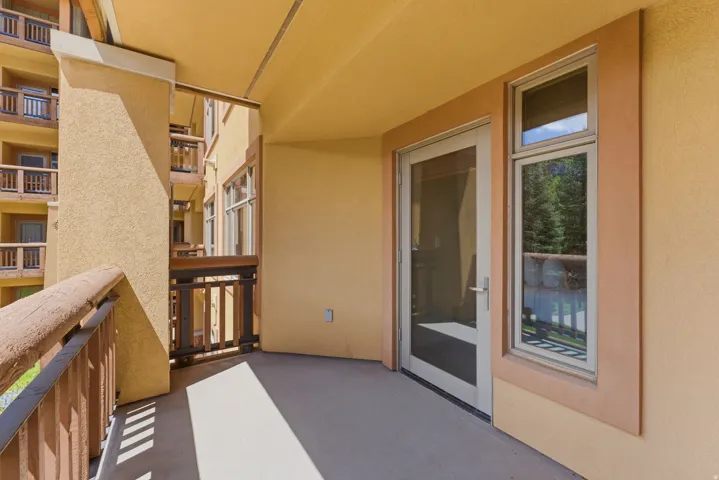 Private balcony with textured stucco exterior, concrete flooring, glass-paneled door, and adjacent vertical window