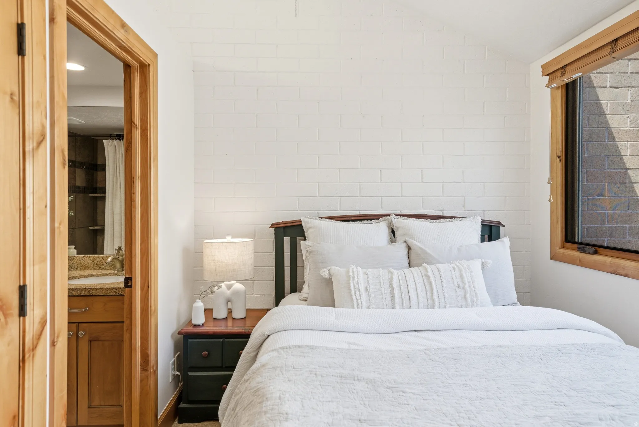 Bedroom featuring a painted brick accent wall and natural wood trim around the window
