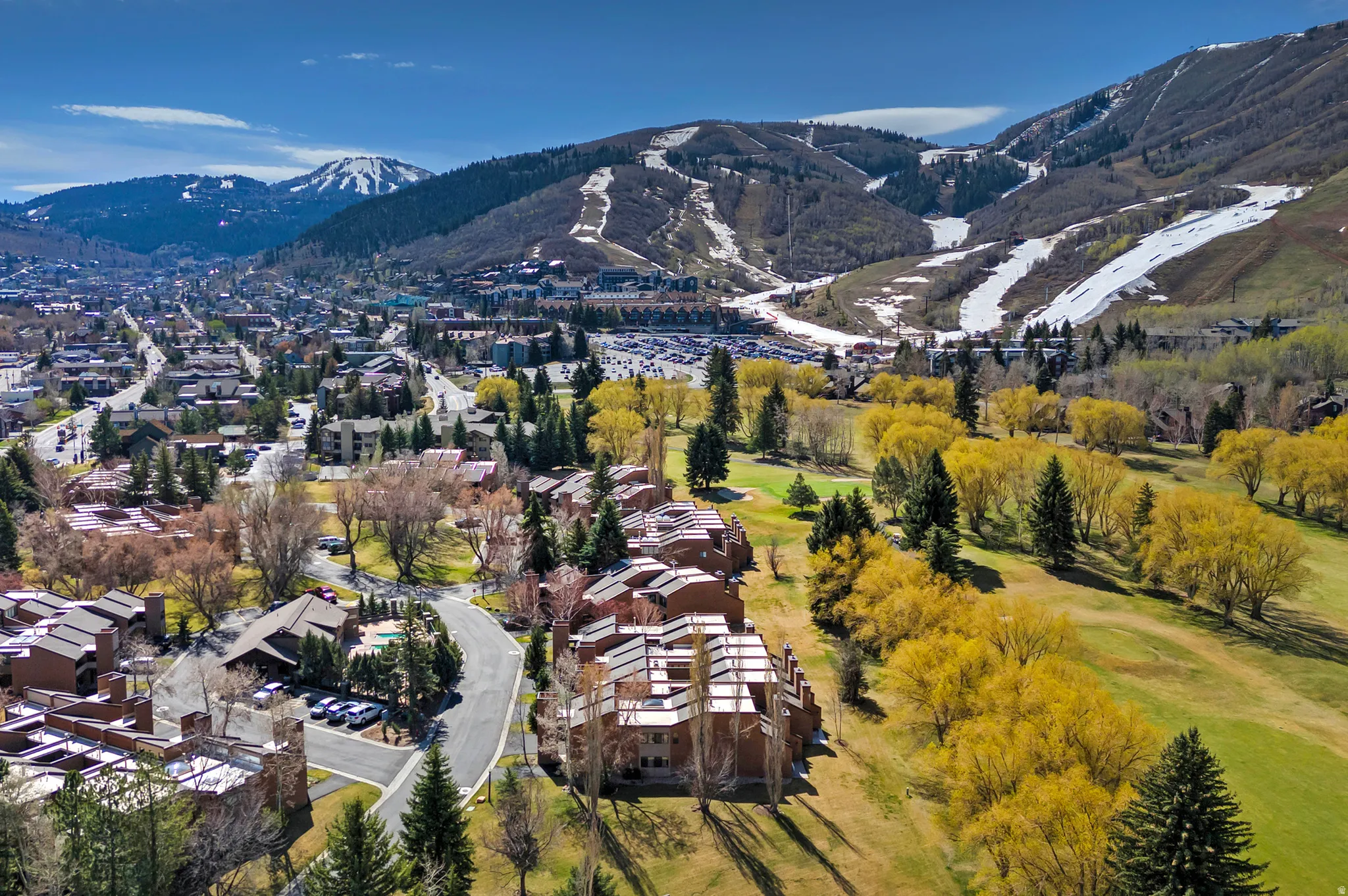 Aerial perspective highlighting the surrounding landscape with mountainous terrain, scattered snow patches, and a developed urban area
