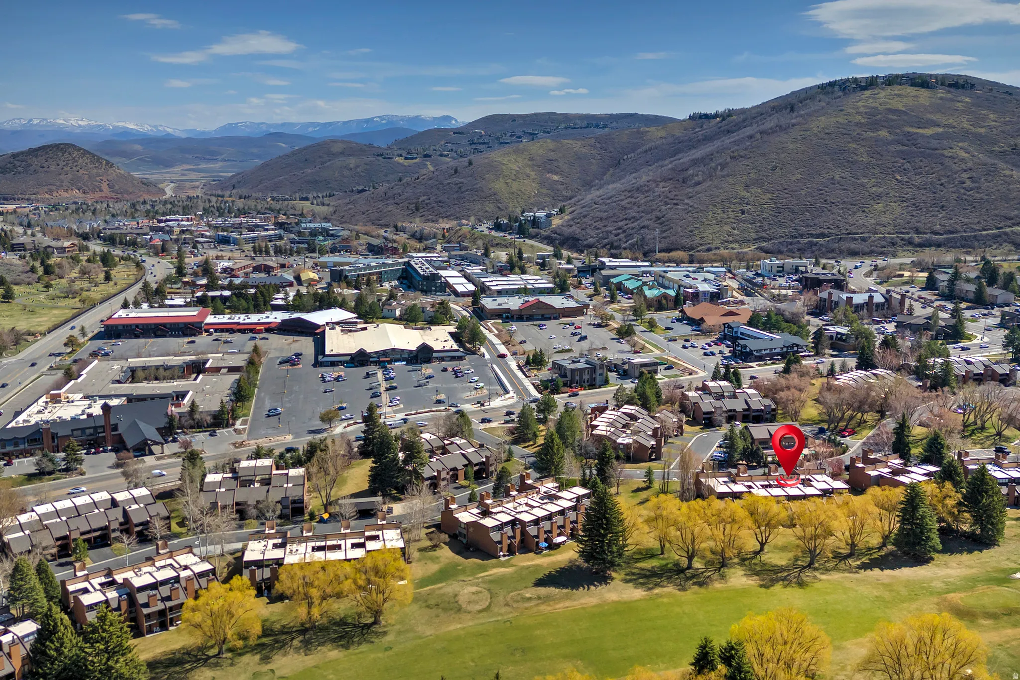 Aerial overview showcasing a golf course perimeter, a collection of residential townhomes, and a commercial district with a large parking area