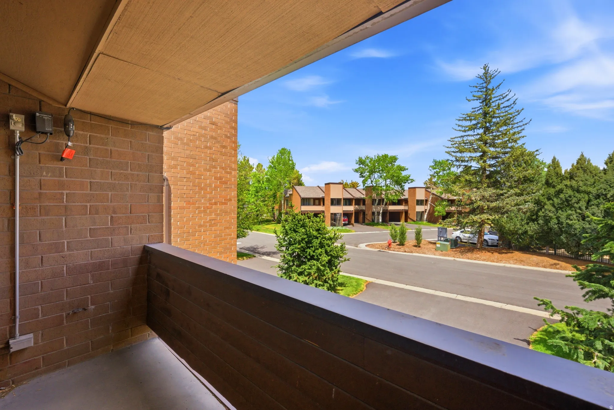 Private balcony with a dark wood-finish railing, brick exterior, and concrete flooring