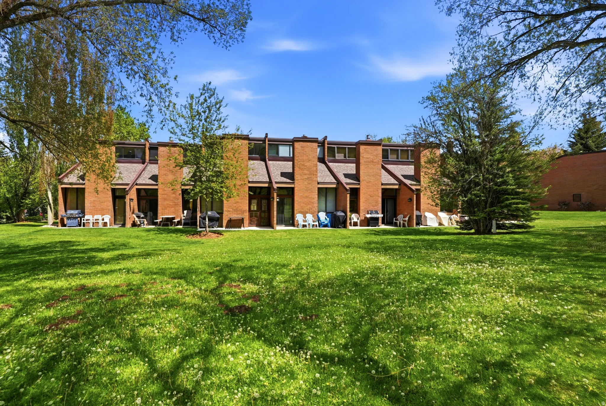 Expansive green space featuring mature trees and a brick facade multi-unit building with individual patios and large windows