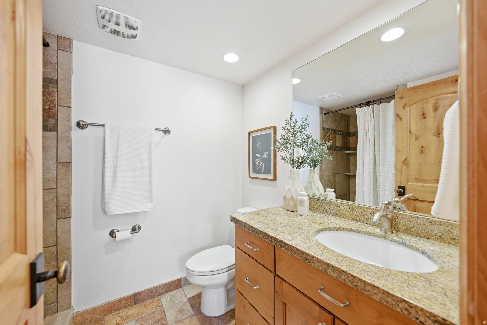 Bathroom featuring a light-toned vanity with an undermount sink, a granite-finish countertop, and wood-finish cabinetry