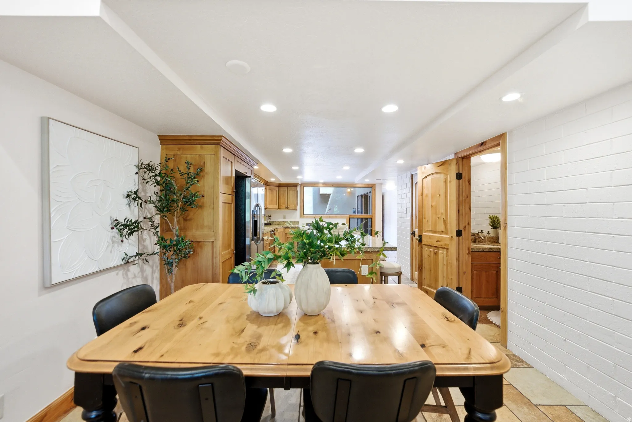 Hardwood dining table with custom turned legs, recessed lighting, white brick accent wall, wood-finish flooring, and natural wood doors