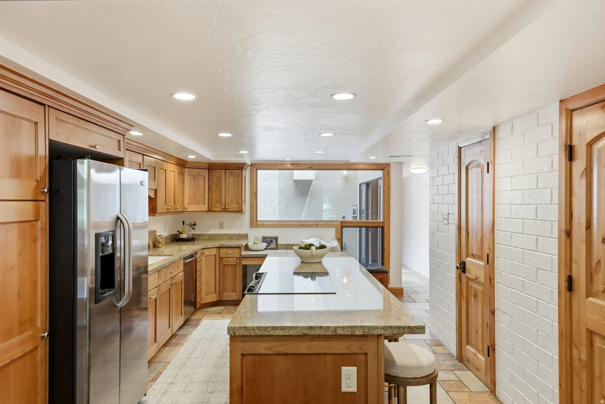 Kitchen featuring wood cabinetry, stainless steel appliances, a center island with a cooktop, stone countertops, and recessed lighting