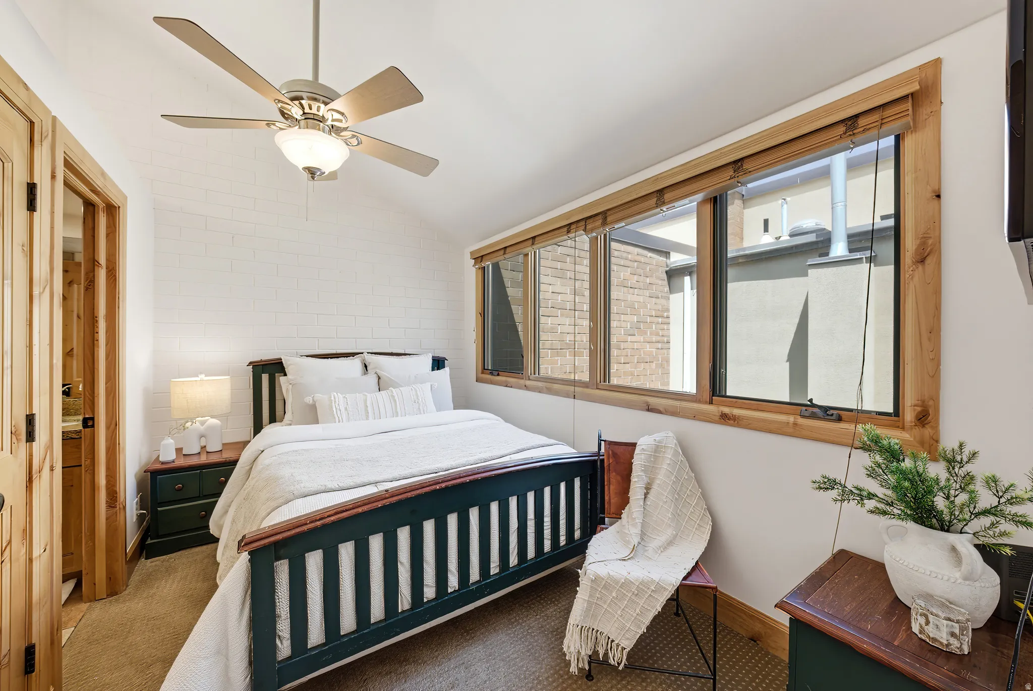 Vaulted ceiling bedroom featuring wood-finish bi-fold doors, a ceiling fan with integrated lighting, a multi-pane window with natural wood trim, and textured white wall finishes