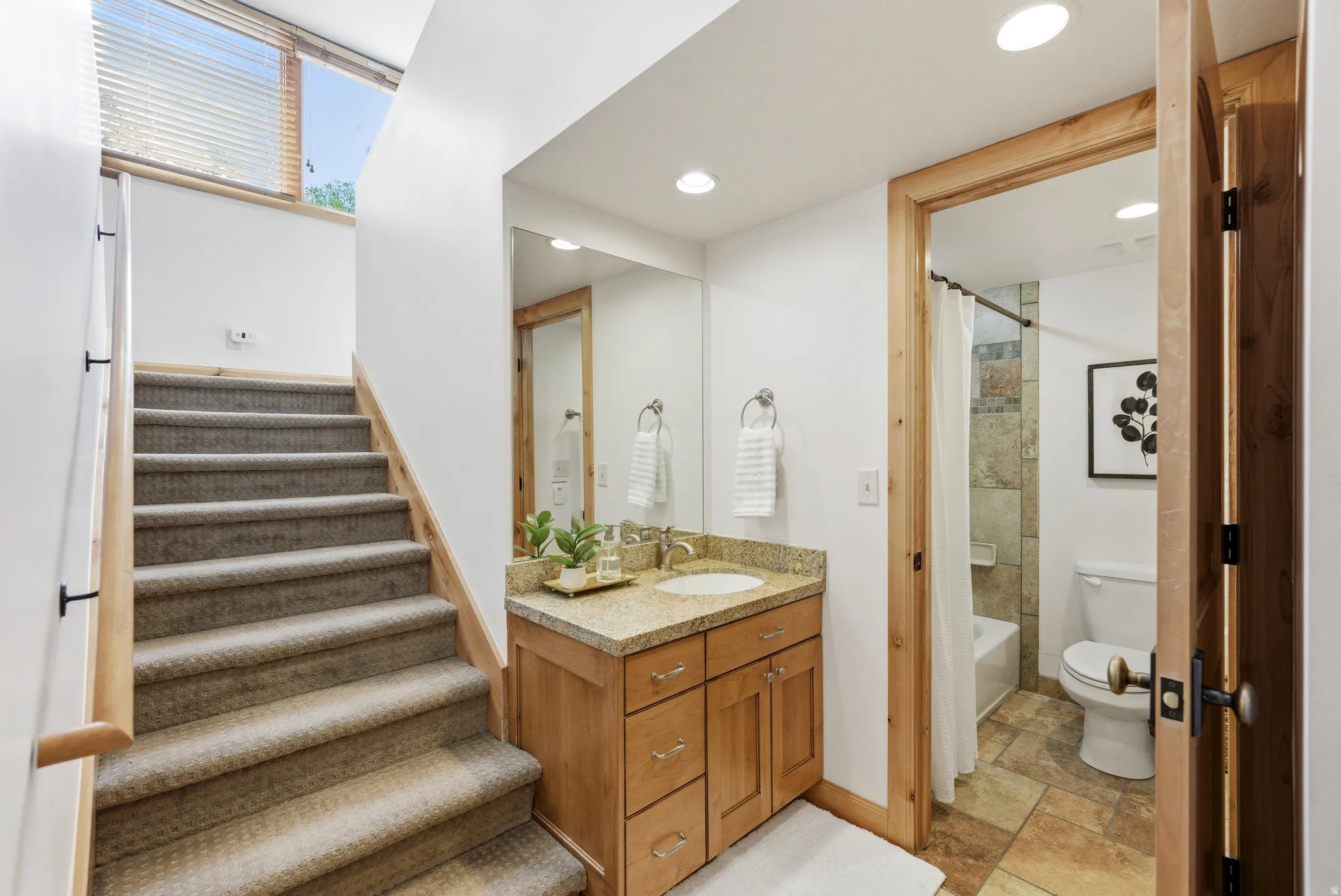 Carpeted staircase with natural wood handrail leading to a brightly lit upper level