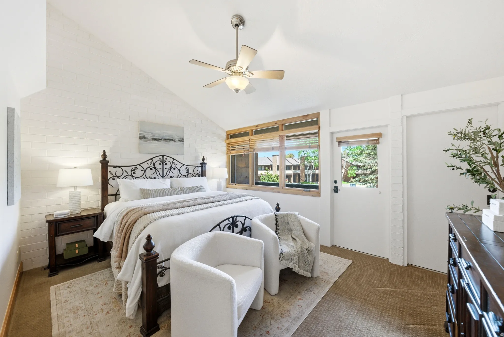 Room featuring a vaulted ceiling with a ceiling fan, white painted brick wall, and wood-framed windows