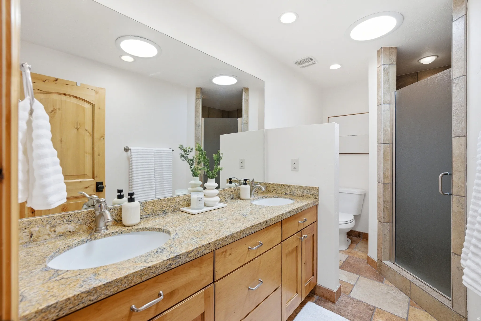 Bathroom featuring a dual vanity with a granite-finish countertop, light wood cabinetry, and brushed nickel hardware