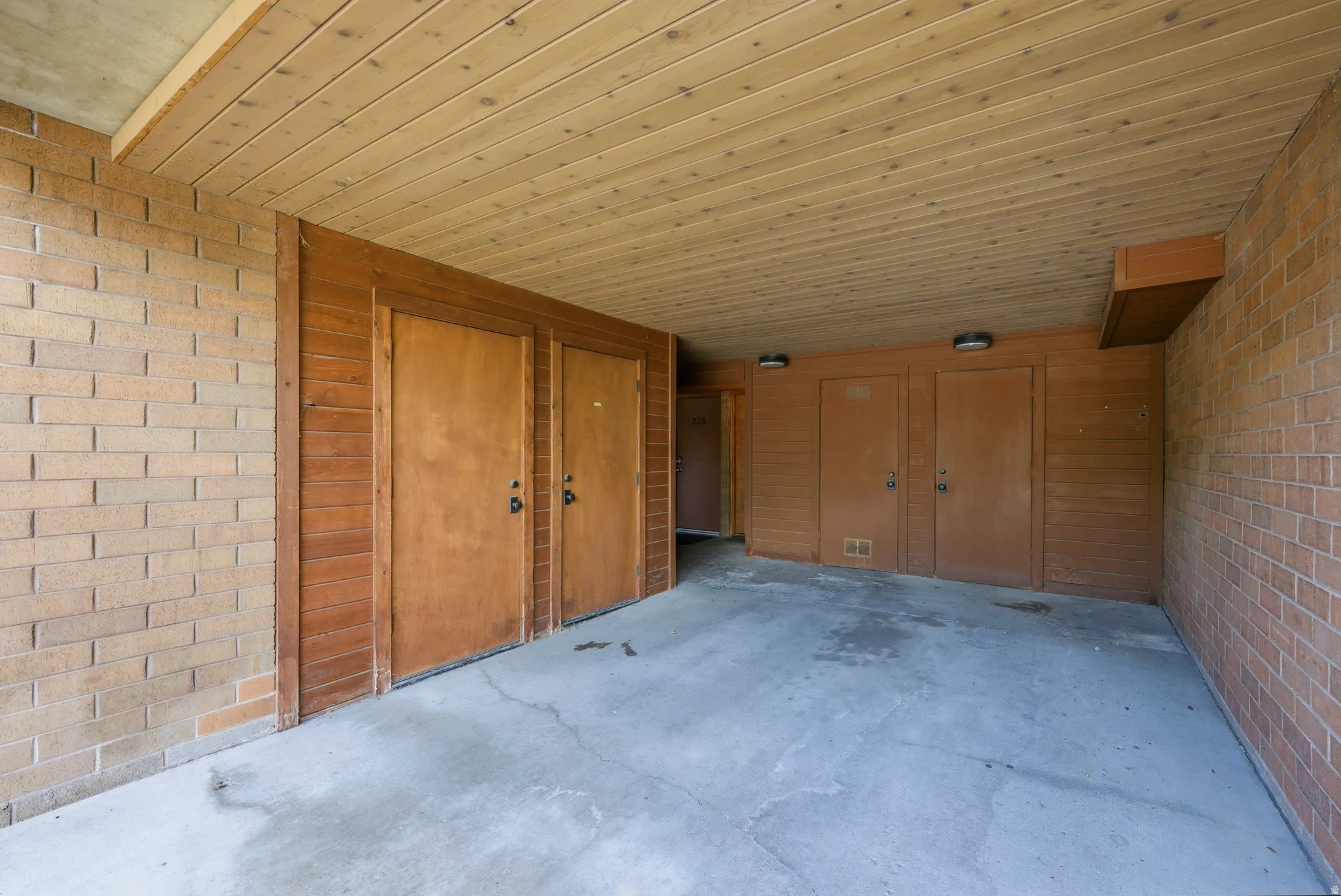 Covered outdoor area featuring a concrete floor, brick walls, and a wood plank ceiling