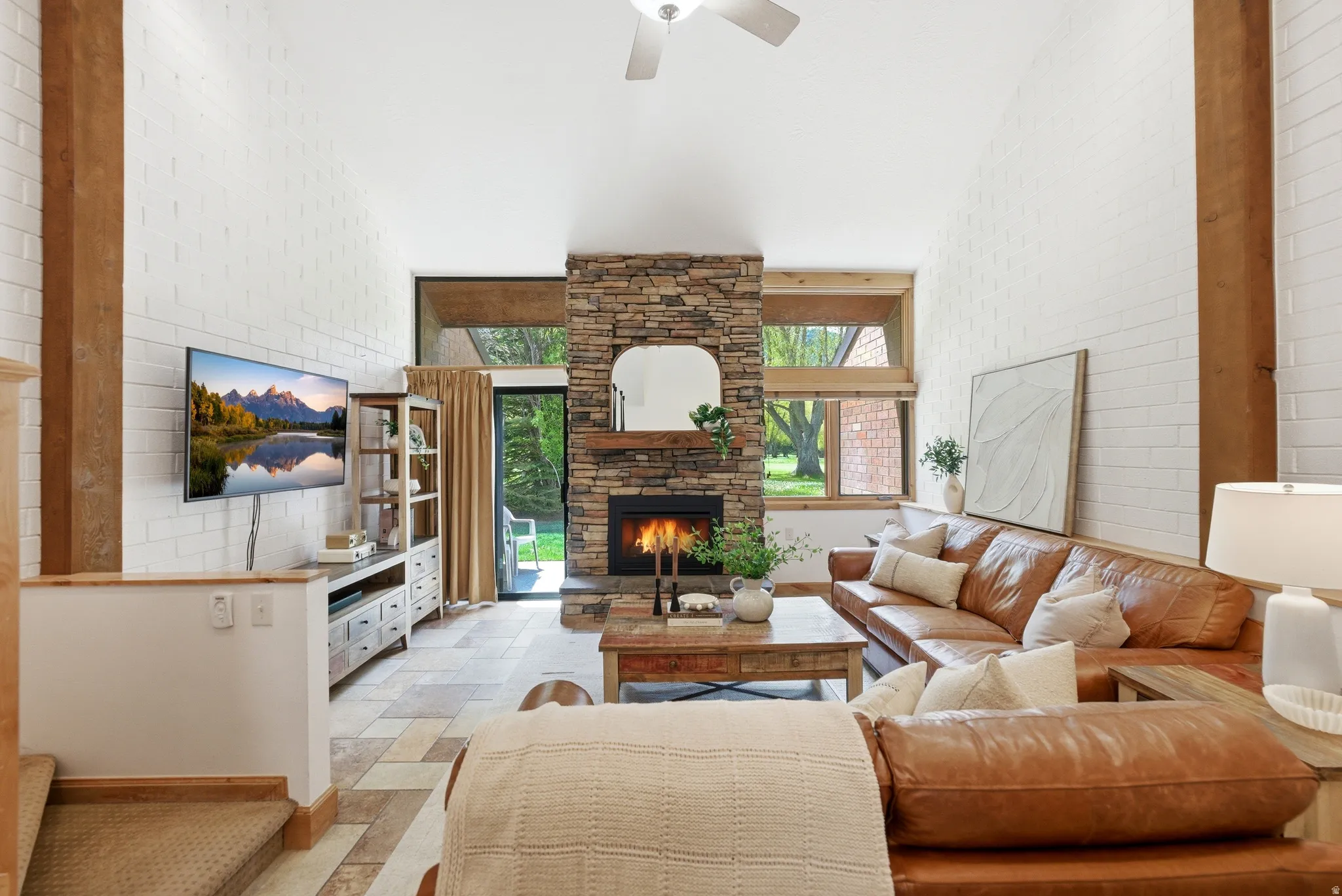Spacious living area featuring a stone fireplace, vaulted ceiling with a ceiling fan, and large windows