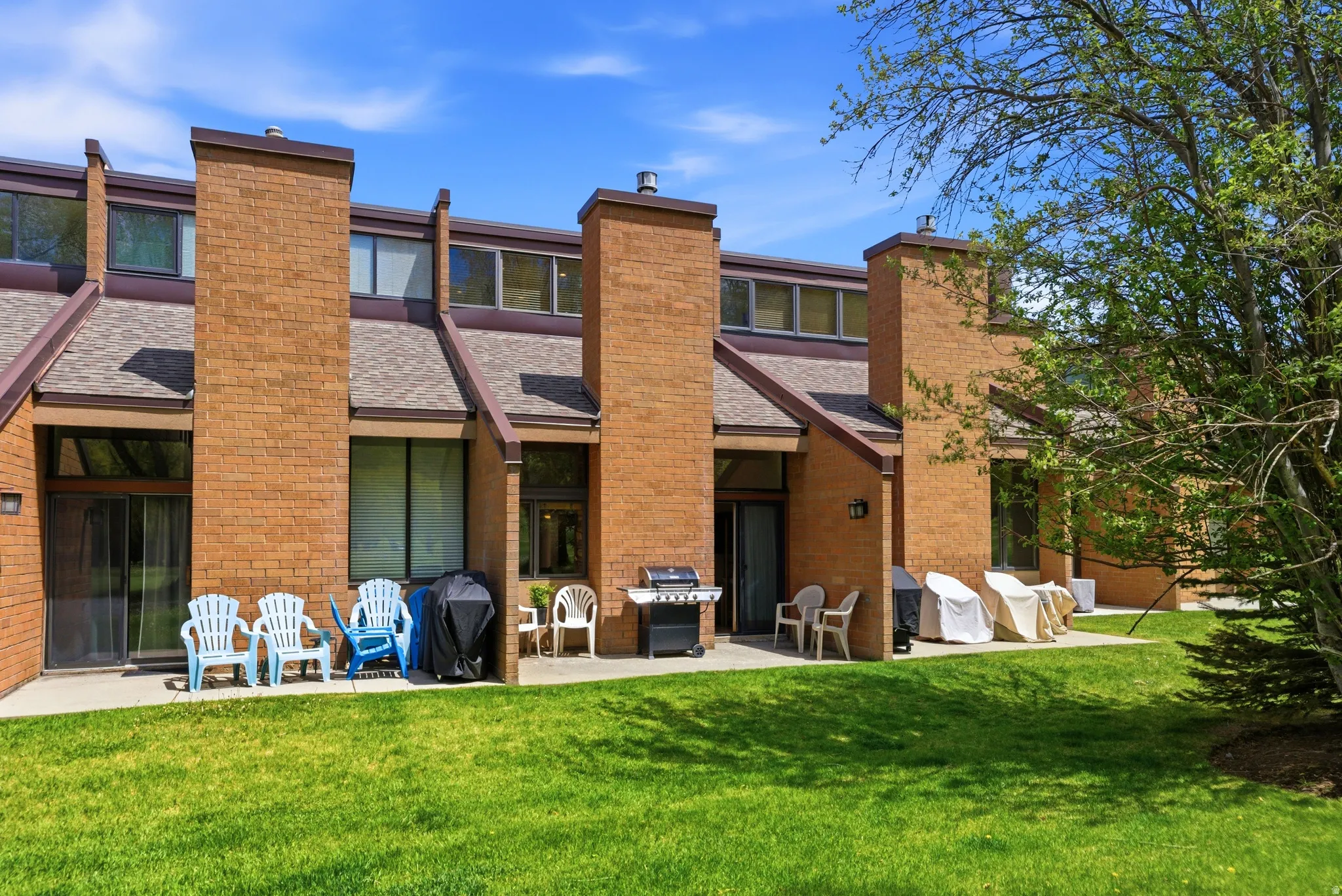 Brick facade townhome with a private patio overlooking a lush green lawn
