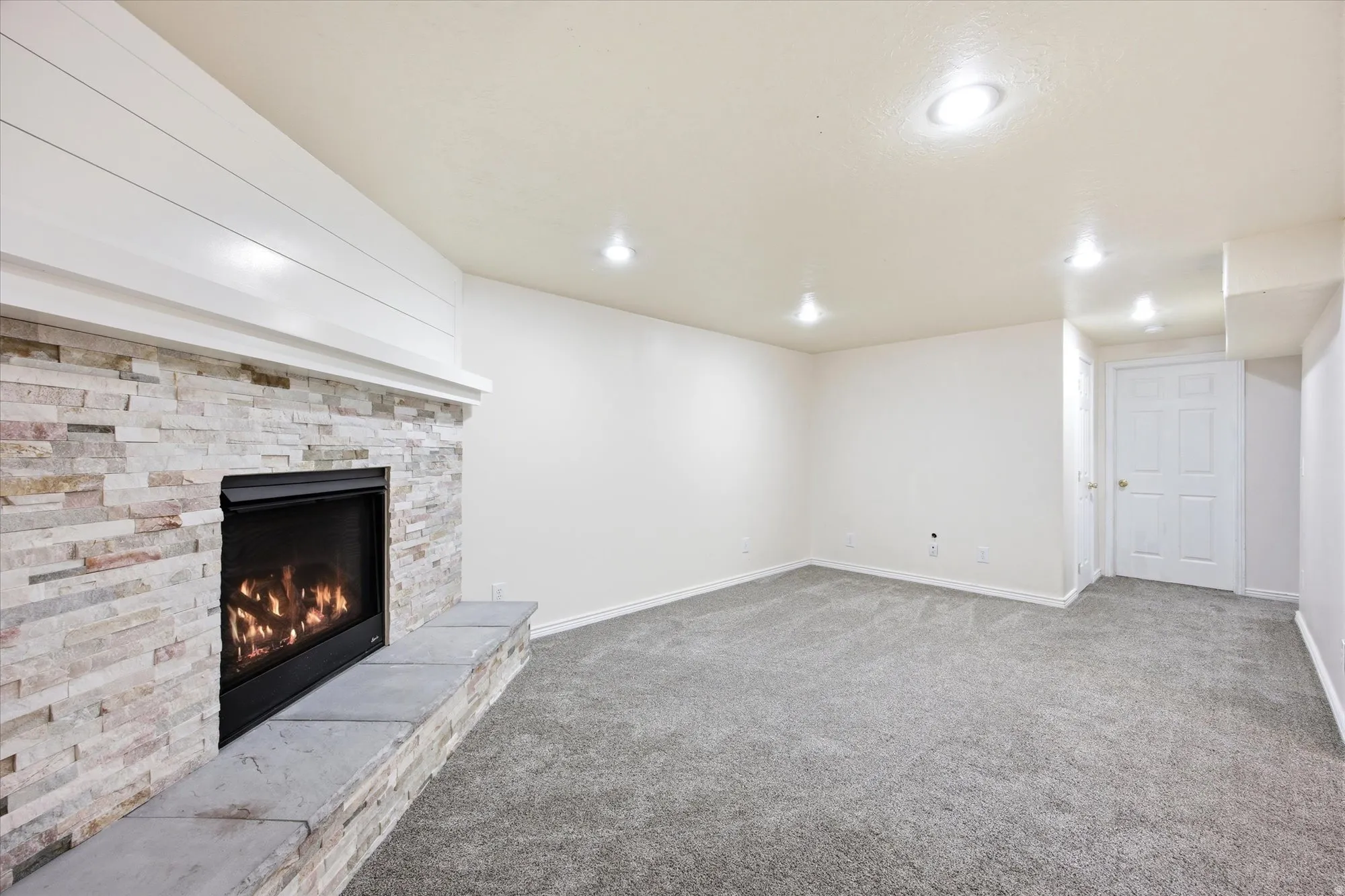Living area featuring a stone-clad gas fireplace with a stone hearth, shiplap-style mantel, recessed lighting, and grey carpet flooring