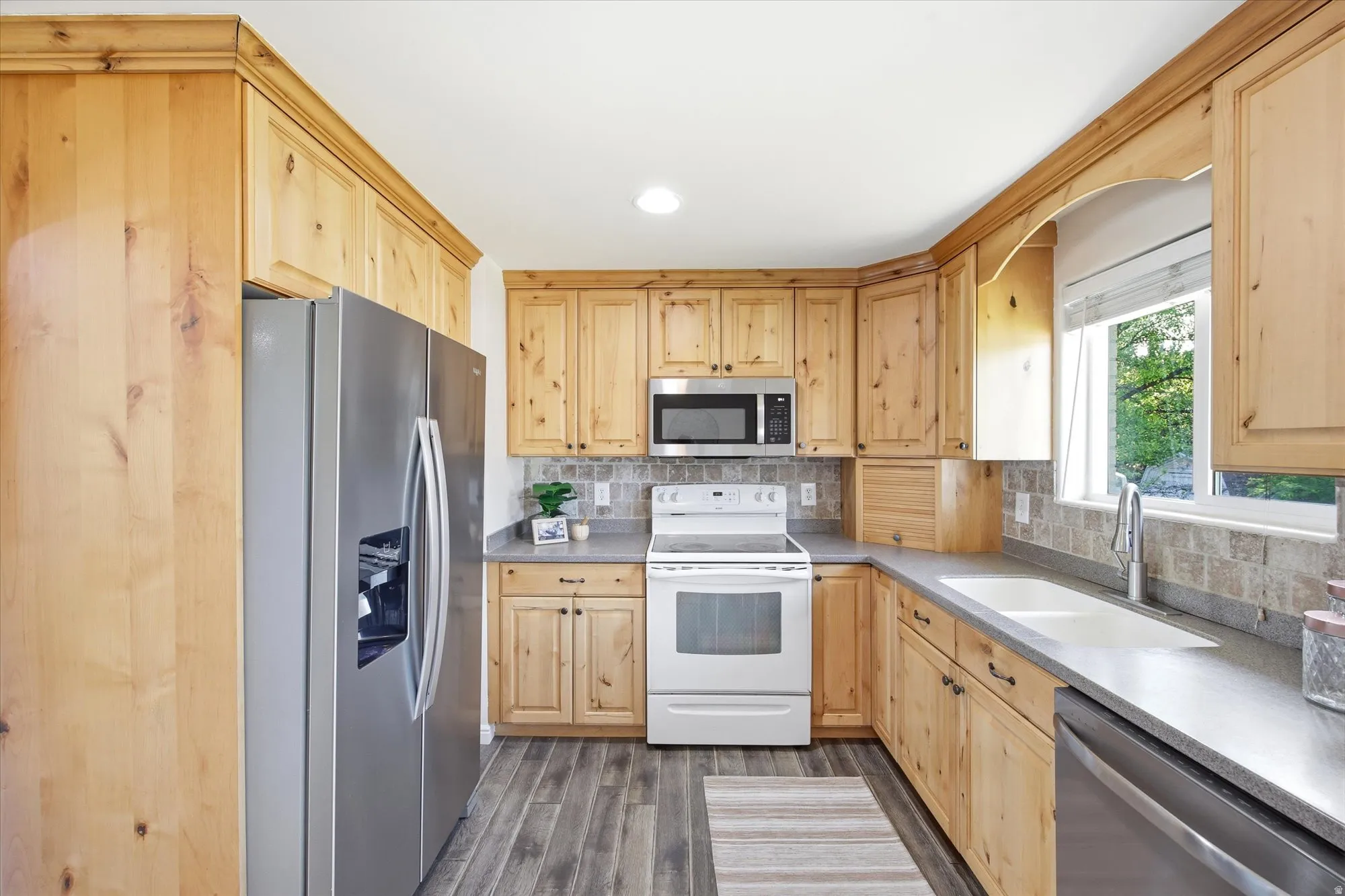 Kitchen featuring light wood cabinetry, corian countertops, stainless steel refrigerator, white smooth top electric range, and wood-finish flooring
