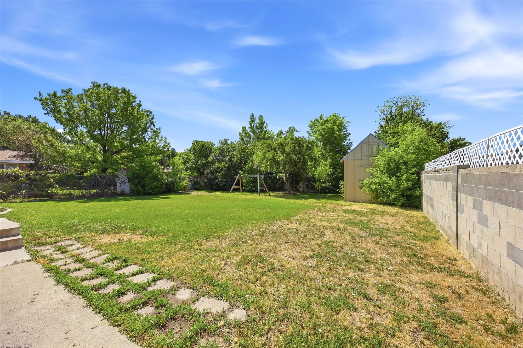 Expansive backyard featuring a partial concrete patio, stepping stones, and a lush lawn