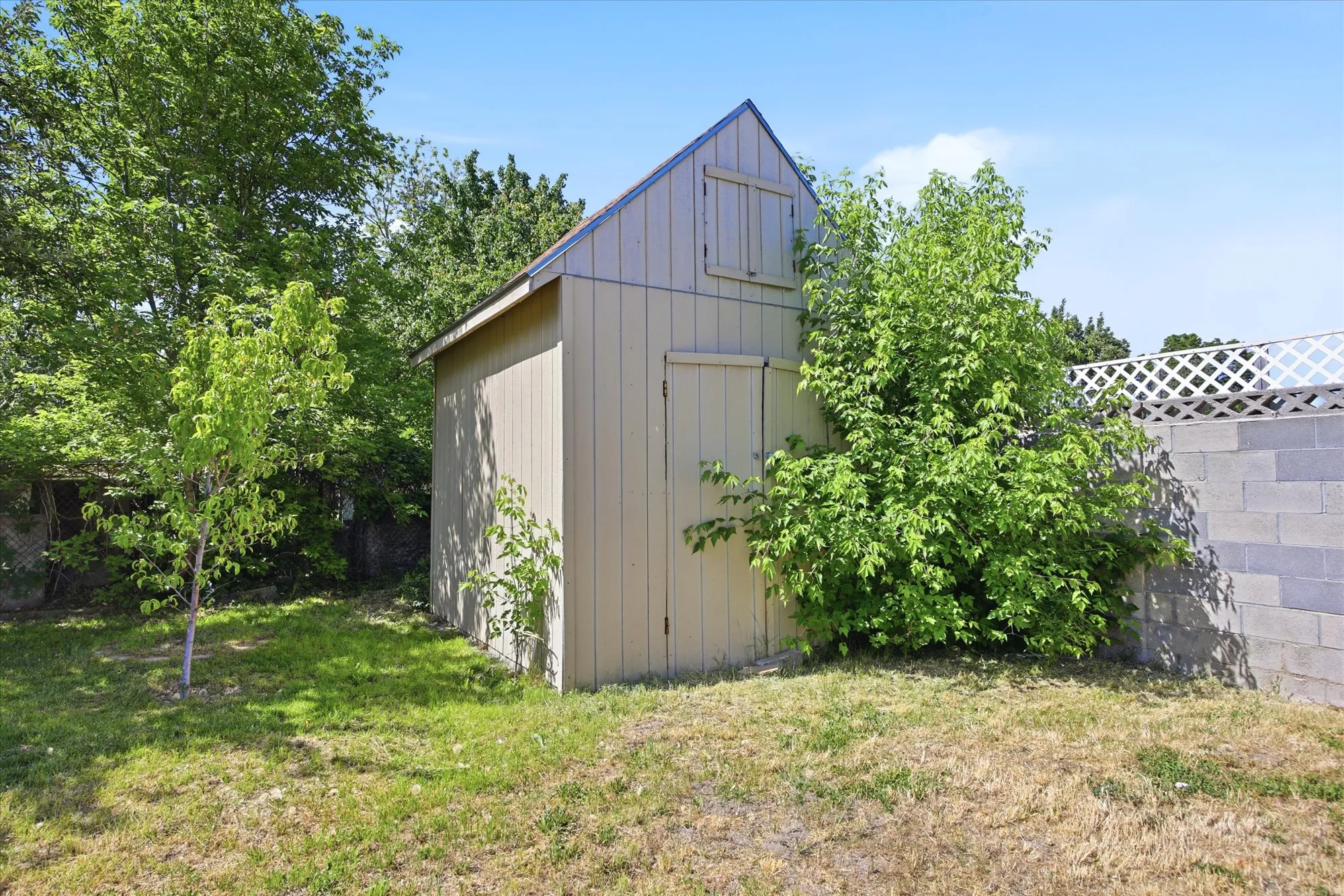 Backyard storage shed featuring a gable roof, double barn doors, and a small upper window
