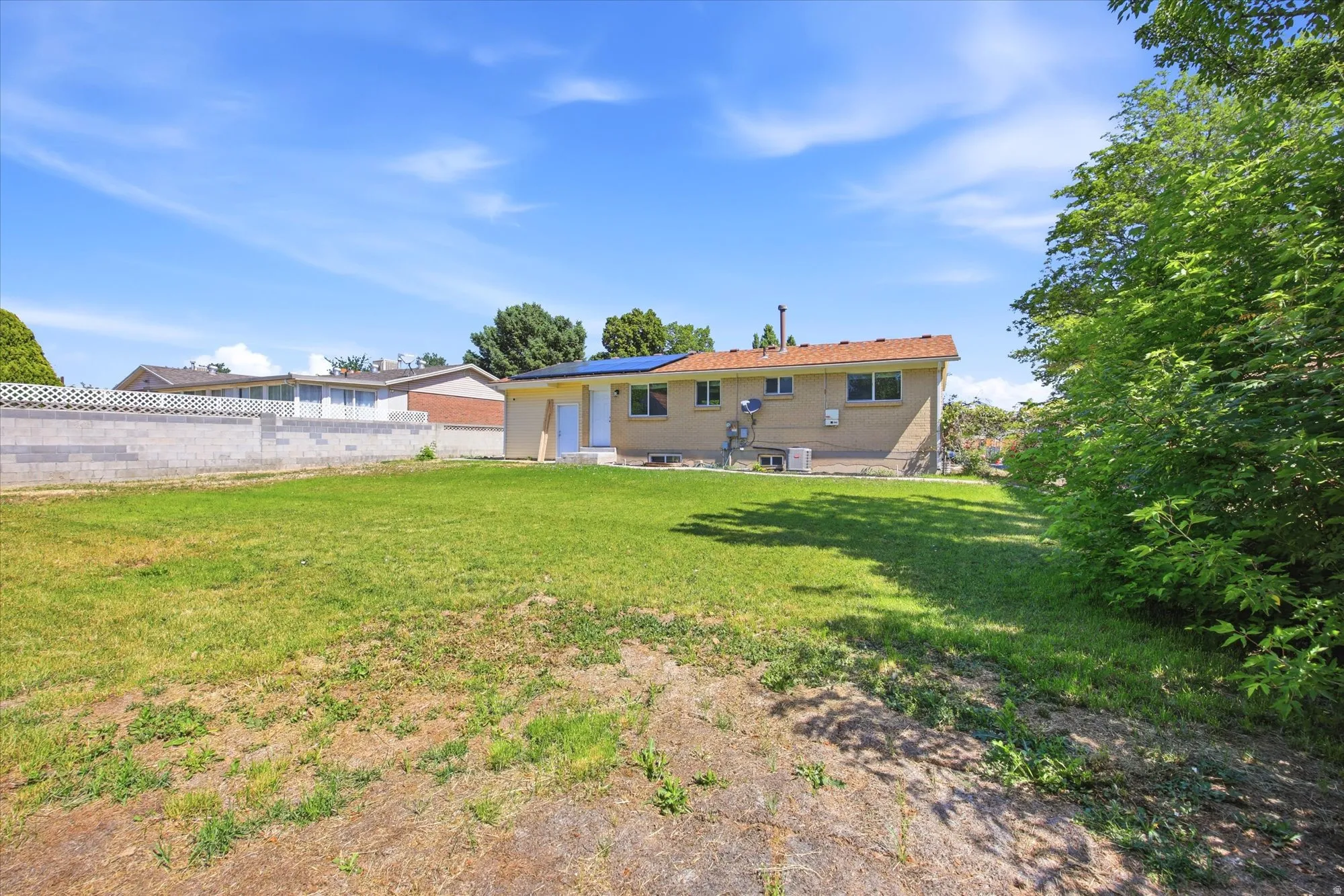 Expansive rear yard featuring green space, mature perimeter trees, and a partial retaining wall