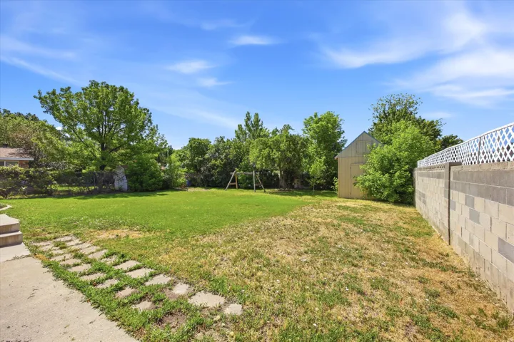 Expansive backyard featuring a partial concrete patio, stepping stones, and a lush lawn
