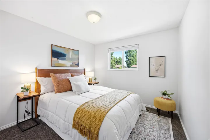 Well-lit room with a window providing natural light, featuring a ceiling-mounted light fixture, a wood-finish headboard, and neutral wall paint