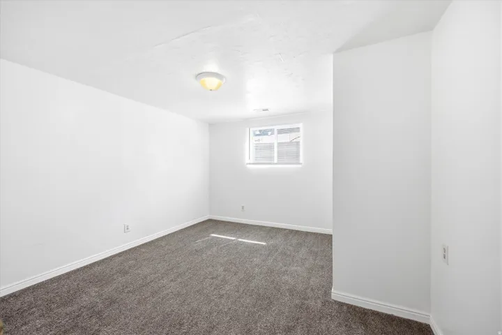Spacious basement bedroom featuring neutral gray carpeting and white baseboards