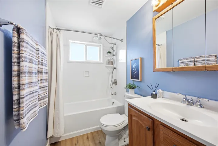Full bathroom featuring a wood-finish vanity with a white countertop and integrated sink, a mirrored medicine cabinet, and a bathtub with an overhead shower and window