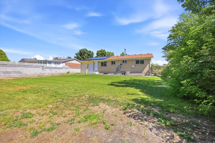 Expansive rear yard featuring green space, mature perimeter trees, and a partial retaining wall