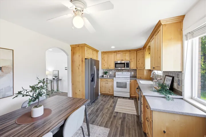 Updated Kitchen featuring wood-finish cabinetry, stainless steel refrigerator, white range, built-in microwave, and a window with blinds
